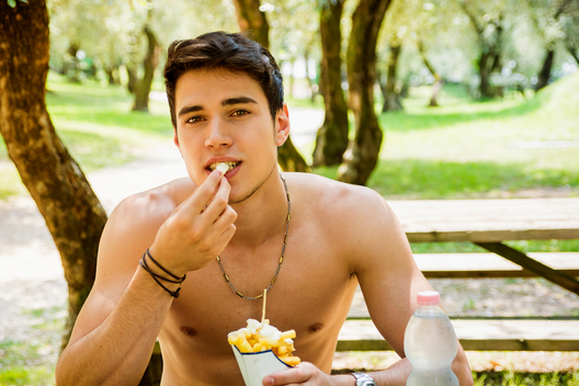 Young Man Having Fast Food Lunch at Picnic Table